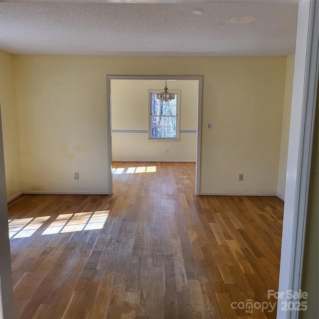 unfurnished room with a textured ceiling, hardwood / wood-style floors, and baseboards