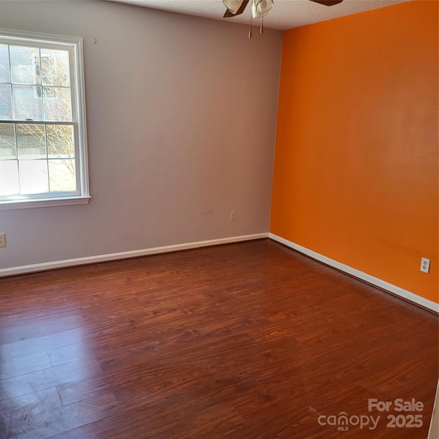 empty room featuring a ceiling fan, baseboards, dark wood finished floors, and a textured ceiling