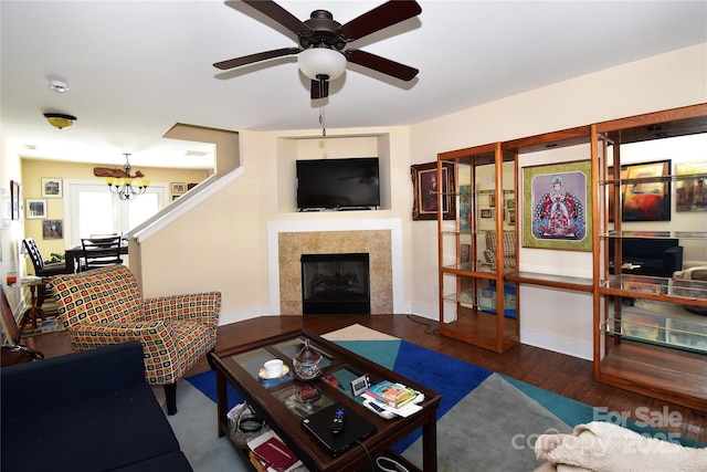 living room with ceiling fan with notable chandelier, a tile fireplace, wood finished floors, and baseboards