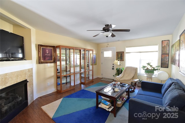 living room with ceiling fan, baseboards, wood finished floors, and a tile fireplace