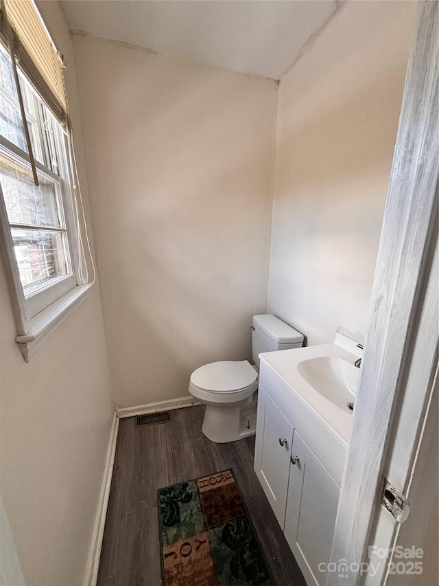 half bath with baseboards, visible vents, toilet, wood finished floors, and vanity