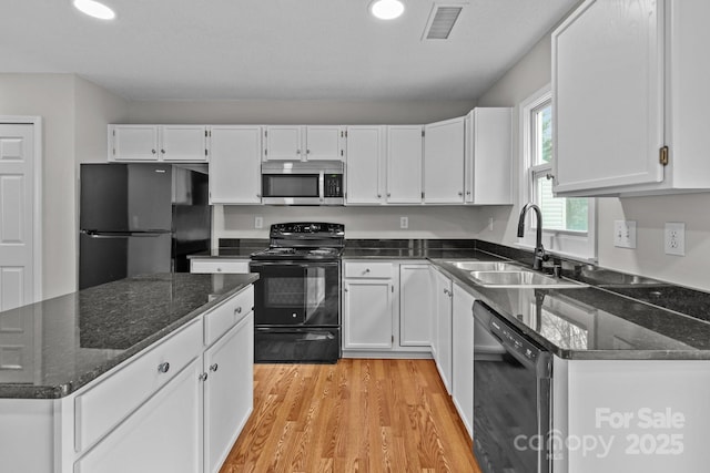 kitchen featuring visible vents, white cabinets, dark stone countertops, black appliances, and a sink