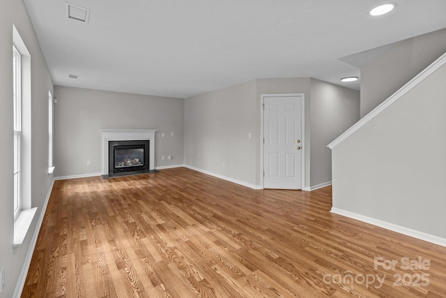 unfurnished living room with a fireplace with flush hearth, wood finished floors, visible vents, and baseboards