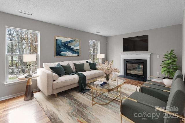 living area featuring a textured ceiling, visible vents, wood finished floors, and a glass covered fireplace