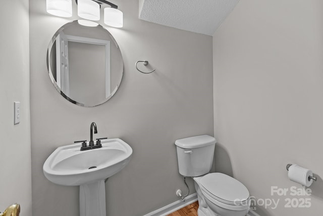 half bathroom with a textured ceiling, toilet, wood finished floors, a sink, and baseboards