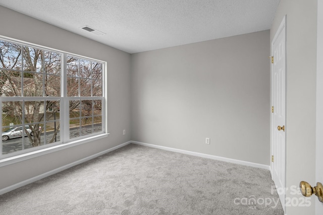 unfurnished room with a textured ceiling, carpet flooring, visible vents, and baseboards