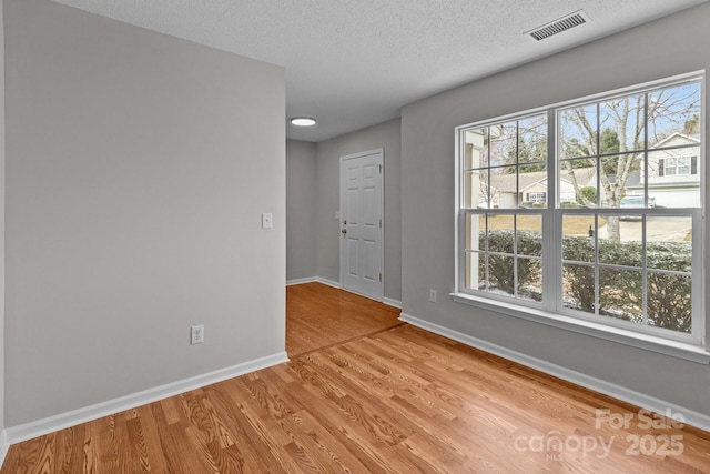 empty room with light wood-style flooring, a healthy amount of sunlight, visible vents, and baseboards