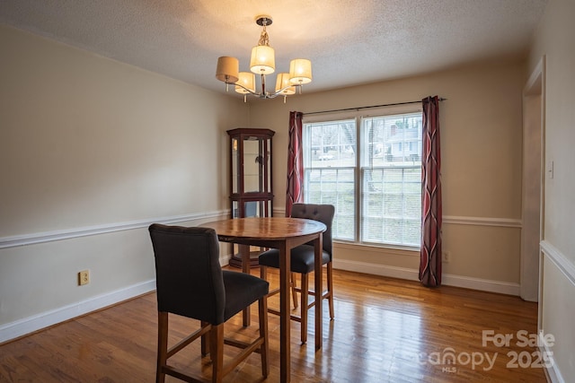 dining area featuring wood finished floors, a textured ceiling, baseboards, and an inviting chandelier