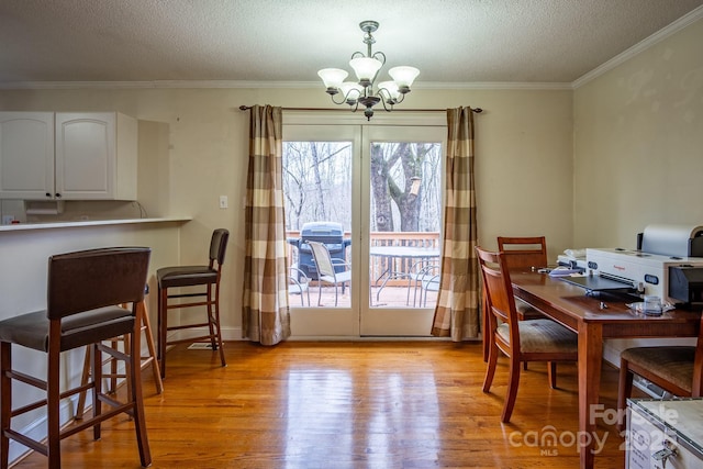 dining area featuring light wood-style flooring, a chandelier, a textured ceiling, and ornamental molding