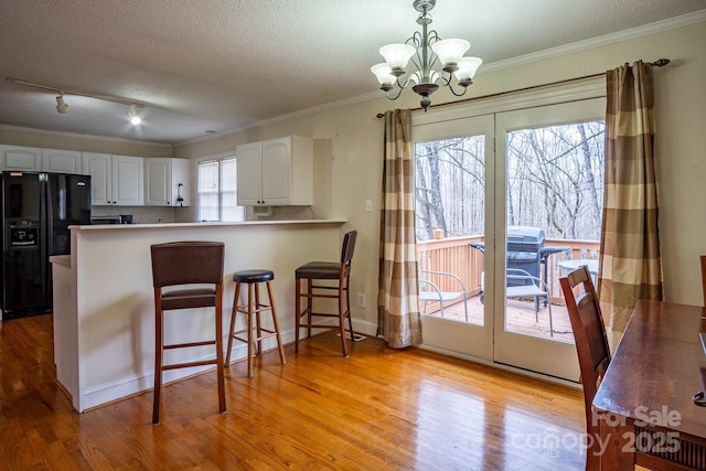 kitchen featuring light wood-style flooring, a peninsula, white cabinetry, hanging light fixtures, and black refrigerator with ice dispenser