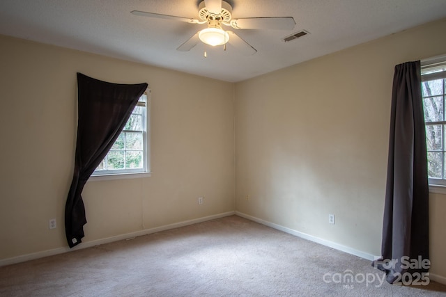 empty room with ceiling fan, light colored carpet, visible vents, and a healthy amount of sunlight