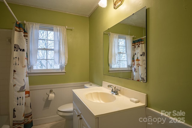 bathroom with a wainscoted wall, toilet, vanity, and shower / tub combo