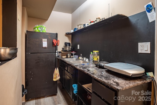 kitchen featuring dark stone countertops, freestanding refrigerator, a sink, and light wood finished floors