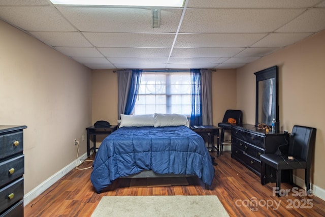 bedroom featuring dark wood-type flooring, a drop ceiling, and baseboards