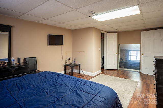 bedroom featuring dark wood-style floors, a drop ceiling, and baseboards