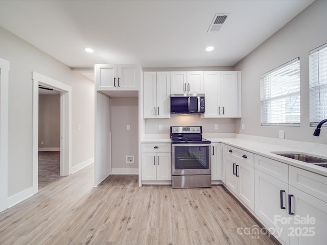 kitchen with visible vents, light wood-style flooring, appliances with stainless steel finishes, white cabinetry, and a sink