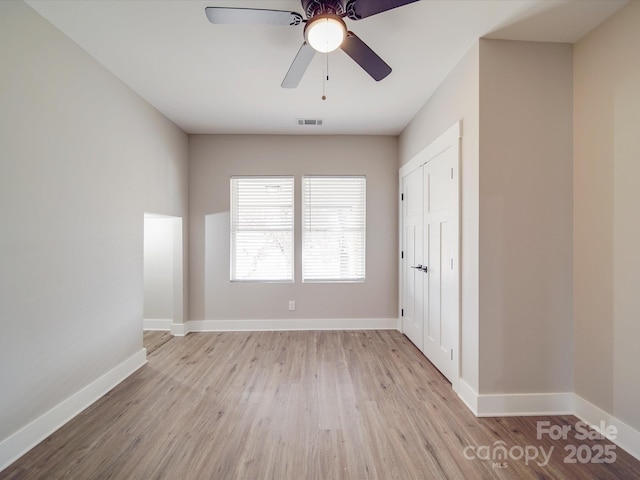 empty room with a ceiling fan, visible vents, baseboards, and wood finished floors