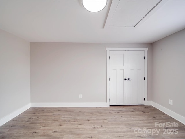 unfurnished bedroom featuring light wood-type flooring, attic access, baseboards, and a closet