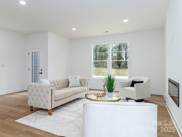 living area with recessed lighting, wood finished floors, and a glass covered fireplace