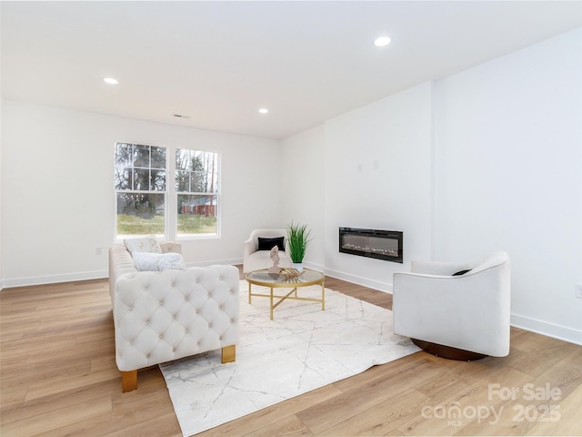 living area with baseboards, wood finished floors, a glass covered fireplace, and recessed lighting