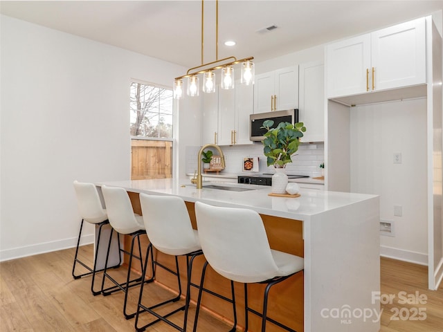 kitchen with stainless steel microwave, visible vents, backsplash, a sink, and light wood-type flooring