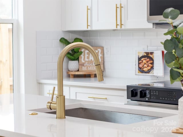 interior details featuring white cabinetry, backsplash, a sink, and light countertops