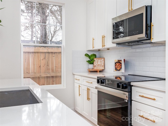 kitchen featuring range with electric stovetop, white cabinets, light countertops, backsplash, and stainless steel microwave