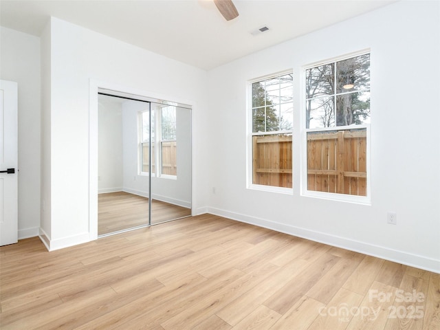 unfurnished bedroom featuring a ceiling fan, visible vents, baseboards, a closet, and light wood finished floors