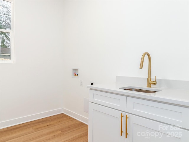 clothes washing area with hookup for an electric dryer, washer hookup, a sink, baseboards, and light wood-type flooring