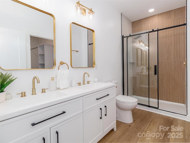 full bathroom with toilet, wood finished floors, a sink, a shower stall, and double vanity