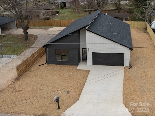 view of front of property with driveway, roof with shingles, an attached garage, and fence