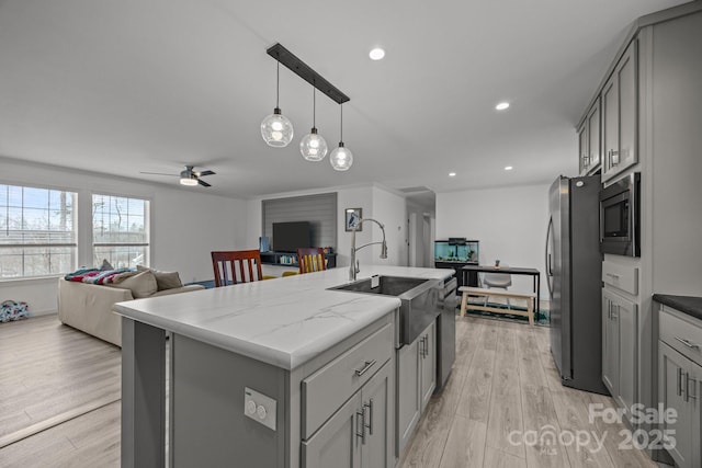 kitchen with a kitchen island with sink, gray cabinetry, stainless steel appliances, open floor plan, and light stone countertops