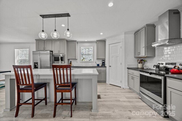 kitchen featuring a breakfast bar, stainless steel appliances, hanging light fixtures, gray cabinetry, and wall chimney range hood