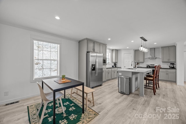 kitchen with a kitchen island with sink, stainless steel appliances, visible vents, light countertops, and wall chimney exhaust hood