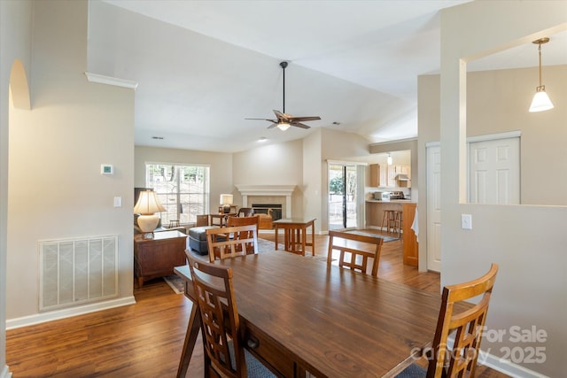 dining room with lofted ceiling, wood finished floors, visible vents, baseboards, and a glass covered fireplace