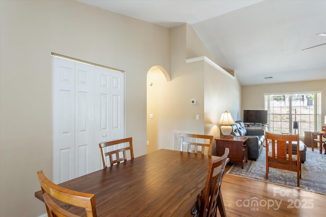 dining space with lofted ceiling, light wood-style flooring, and arched walkways