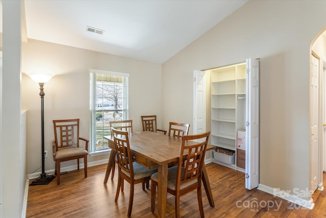 dining area featuring vaulted ceiling, arched walkways, wood finished floors, and visible vents