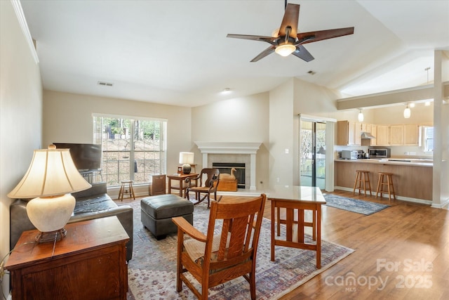 living area featuring lofted ceiling, a tile fireplace, visible vents, a ceiling fan, and light wood finished floors