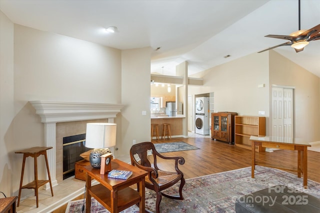 living area with a fireplace, stacked washer / drying machine, a ceiling fan, vaulted ceiling, and light wood-type flooring