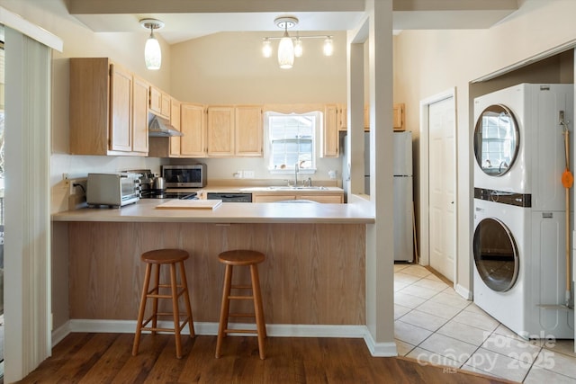 kitchen featuring light brown cabinets, a peninsula, light countertops, stacked washing maching and dryer, and stainless steel microwave