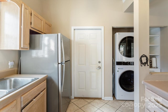 interior space featuring light tile patterned flooring, light brown cabinets, stacked washer / drying machine, light countertops, and freestanding refrigerator