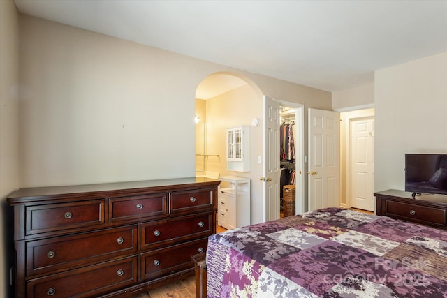 bedroom with arched walkways, connected bathroom, a closet, light wood-type flooring, and a walk in closet