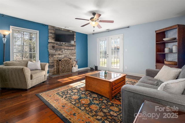 living room with a healthy amount of sunlight, dark wood finished floors, a stone fireplace, and french doors