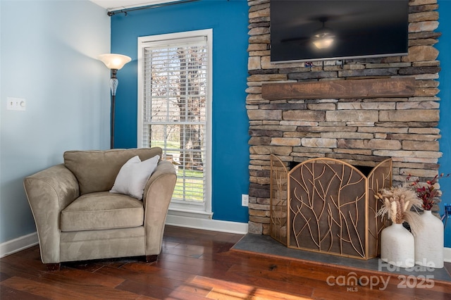 sitting room featuring a stone fireplace, hardwood / wood-style floors, and baseboards