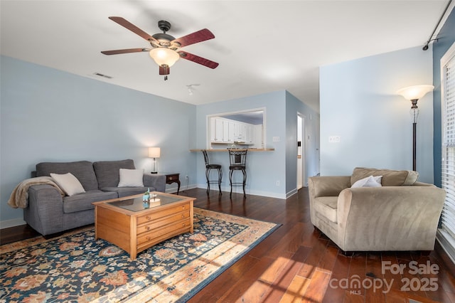 living area featuring a ceiling fan, dark wood finished floors, visible vents, and baseboards