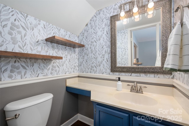 bathroom with toilet, vaulted ceiling, vanity, and wallpapered walls