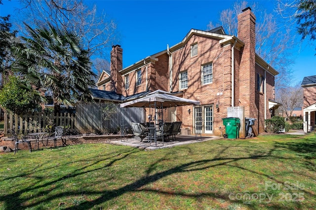 rear view of property featuring a yard, brick siding, a chimney, and fence