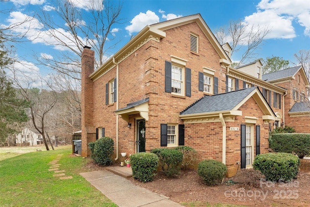 view of front of house featuring brick siding, a chimney, a shingled roof, and a front lawn