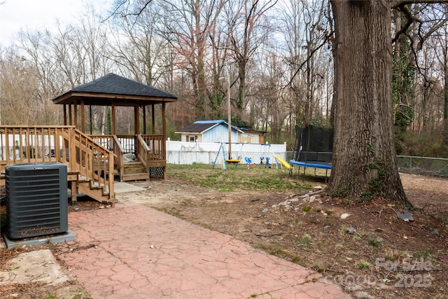 view of yard with a fenced backyard, a trampoline, a gazebo, central AC, and a playground