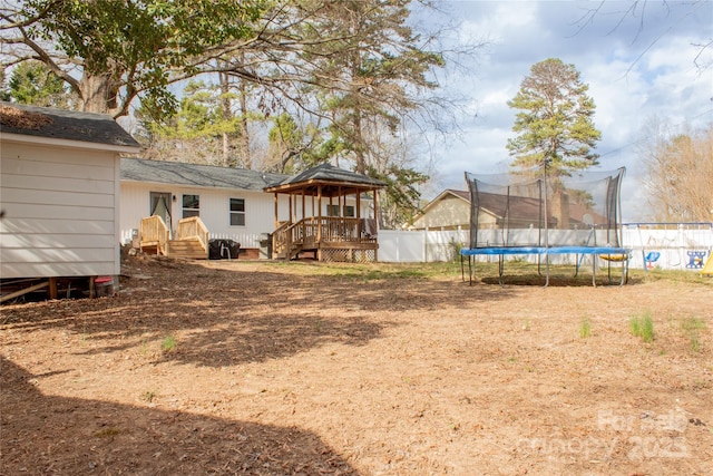 view of yard with a gazebo, a trampoline, fence, and a wooden deck